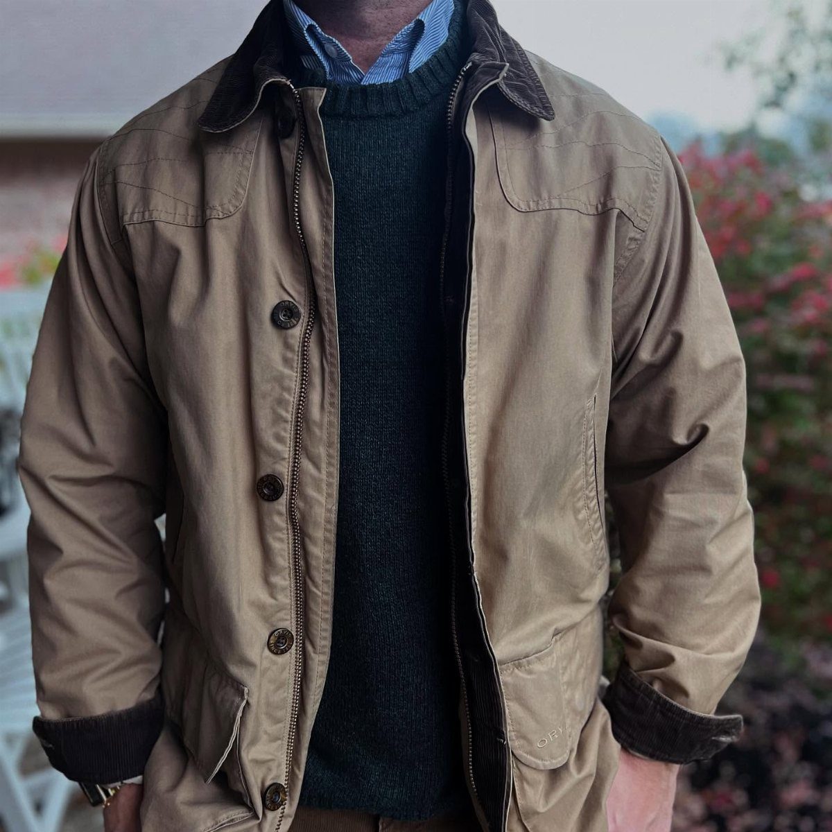 Tan field coat with brown collar worn over a green sweater and blue shirt.