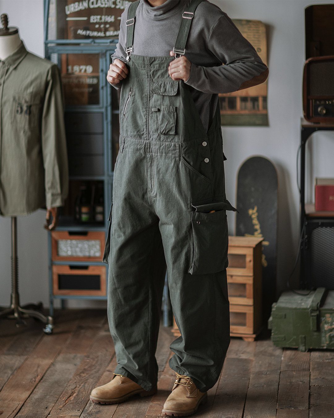 Person wearing olive green bib overalls and tan boots in a rustic room