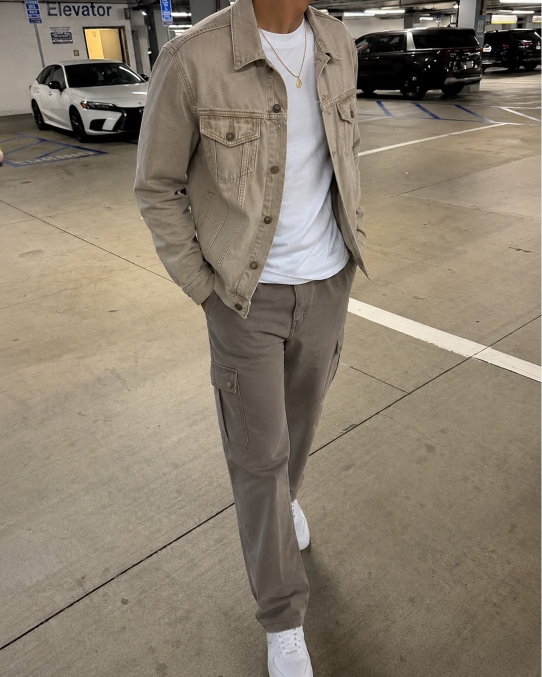 Person wearing a tan denim jacket and taupe cargo pants in a parking garage.