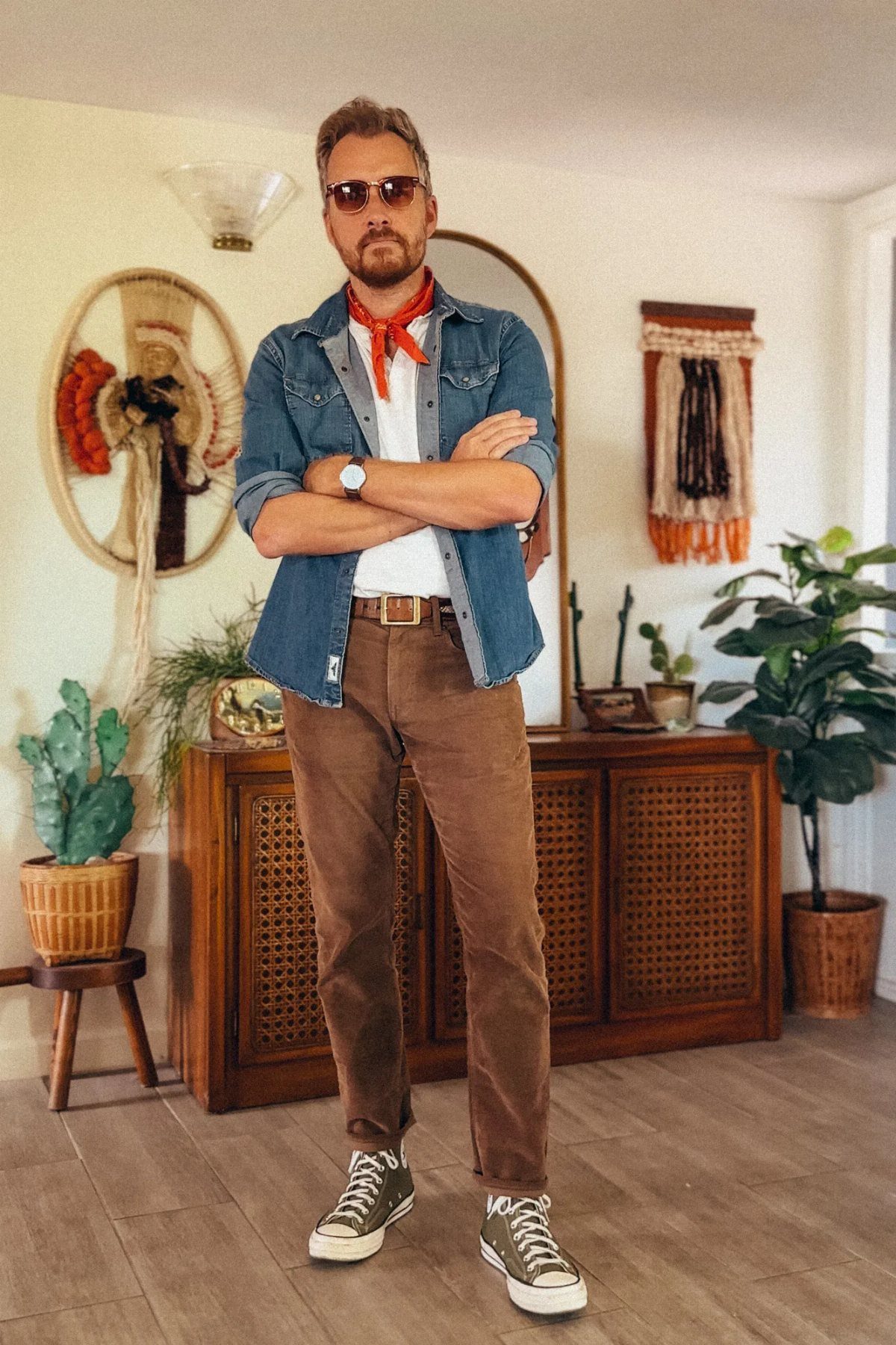 Man wearing a blue denim jacket and brown corduroy pants in a living room.