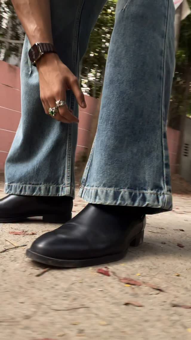 Light-wash blue flare jeans paired with black leather boots on a concrete ground.
