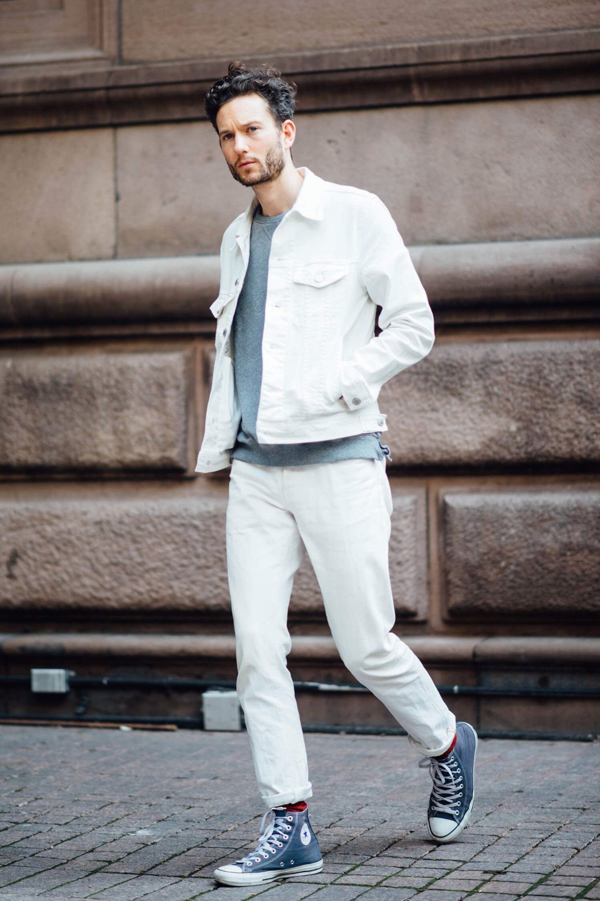 Man wearing a white denim jacket and white jeans with blue sneakers.