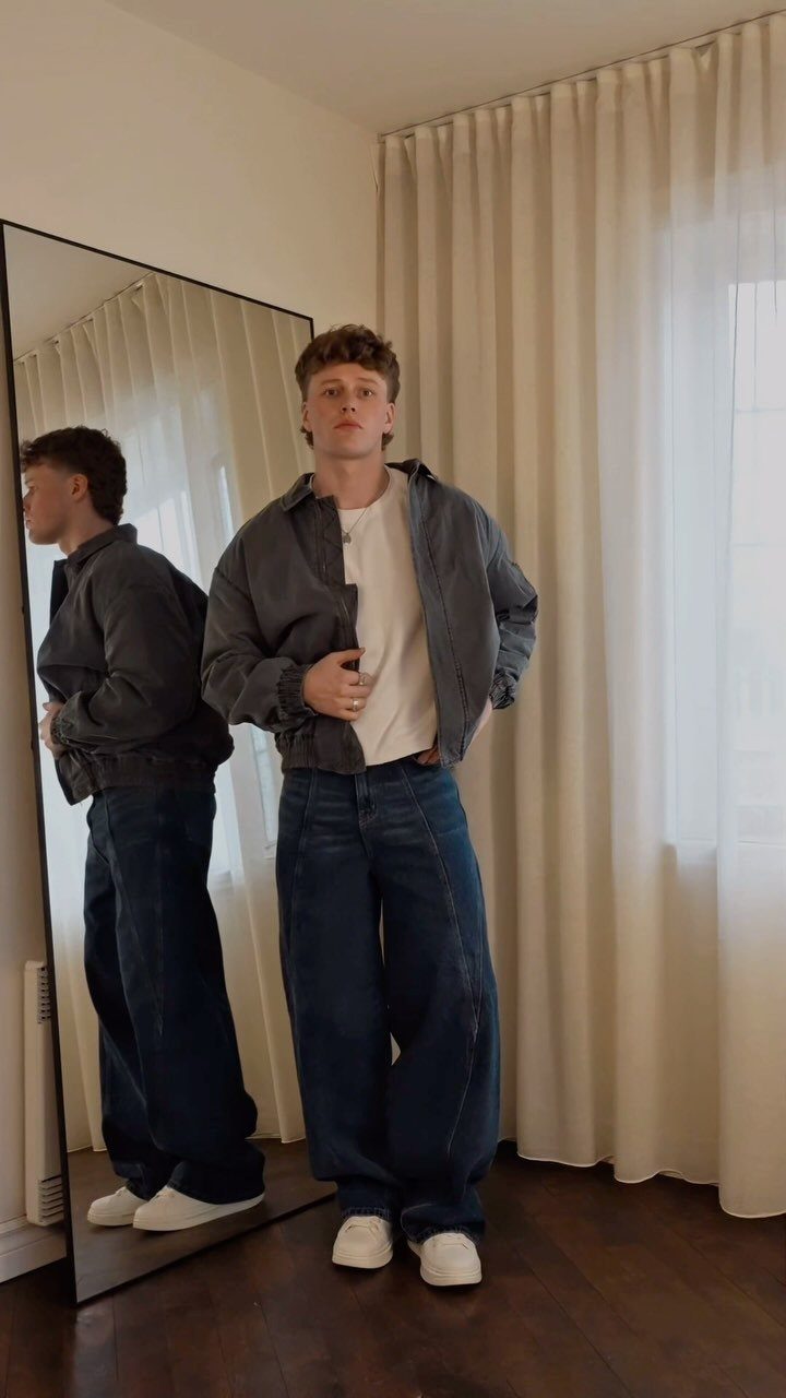 Man wearing a blue denim jacket and wide-leg dark blue jeans with white sneakers.