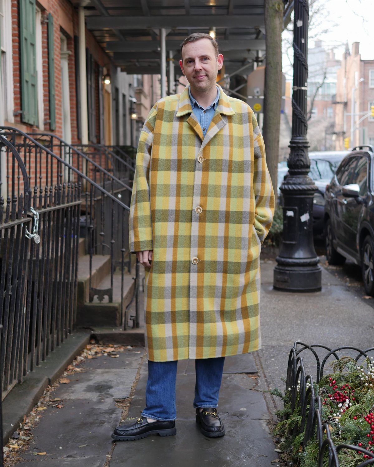 Man wearing a yellow and grey large-check plaid trench coat on a city street