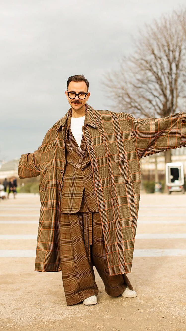 Man wearing an oversized brown plaid trench coat and matching plaid suit outdoors.