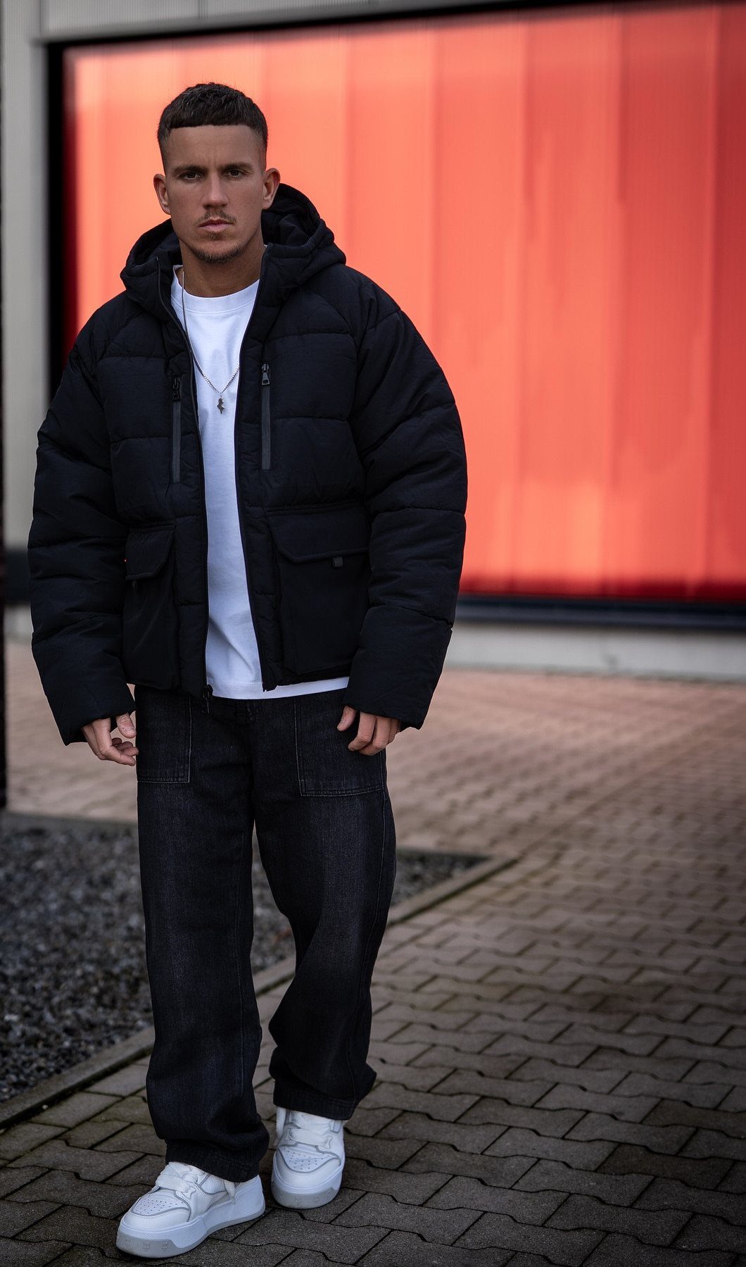 Man wearing a black puffer jacket, white t-shirt, black jeans, and white sneakers.