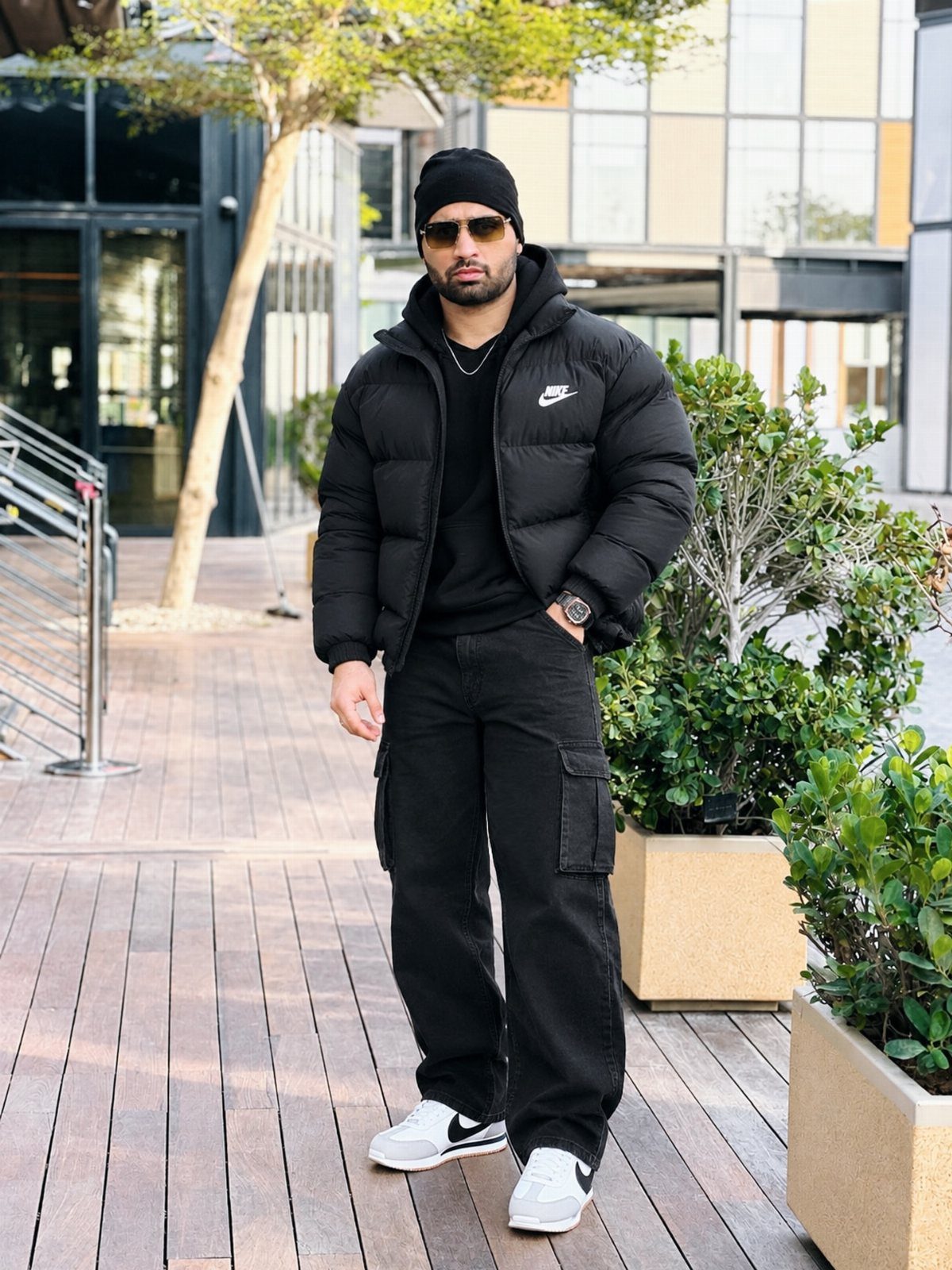Man wearing black puffer jacket, black cargo pants, and white sneakers on wooden deck