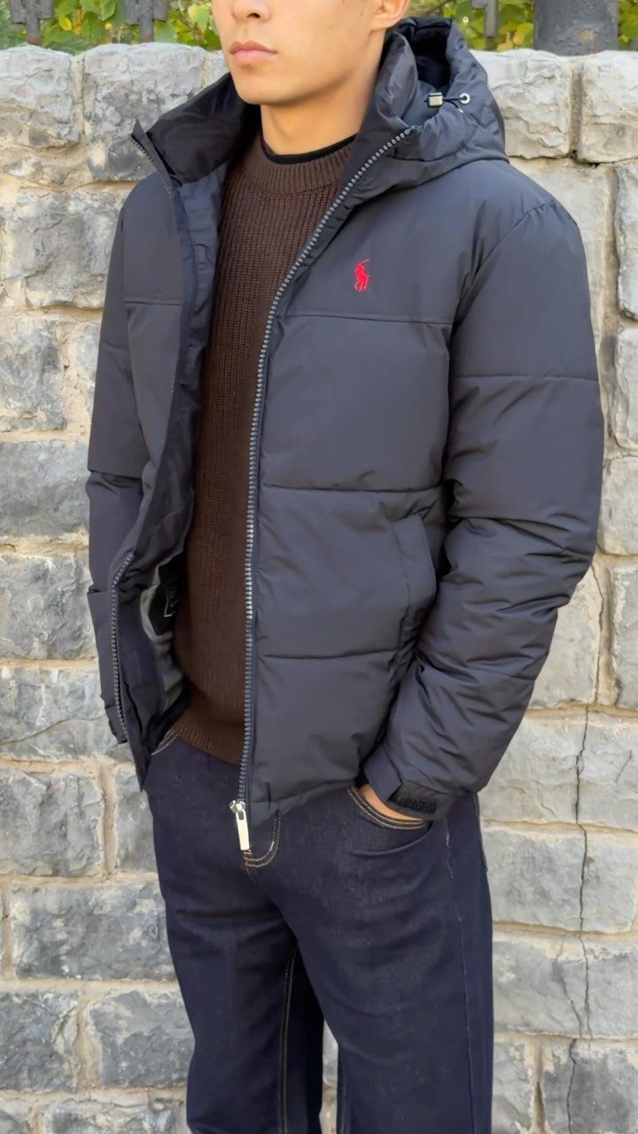 Man wearing a black puffer jacket, brown knit sweater, and navy blue jeans.