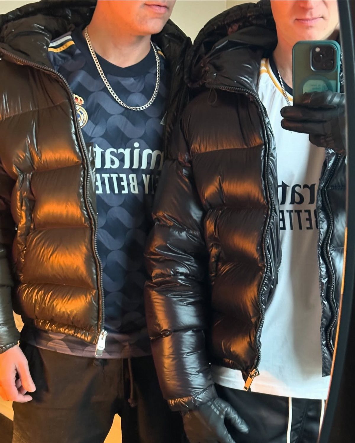 Two men in shiny black puffer jackets and sports jerseys posing for a selfie.