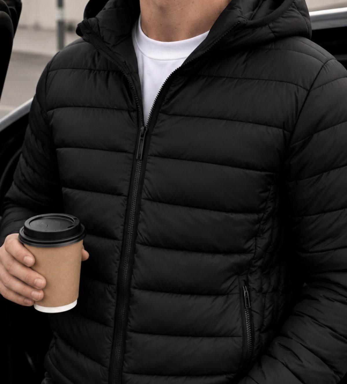 Man in black puffer jacket and white t-shirt holding a coffee cup