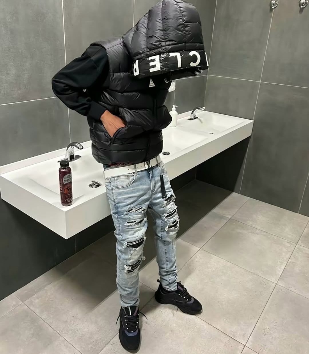 Man wearing a black puffer vest, black hoodie, and distressed slim light-wash jeans.