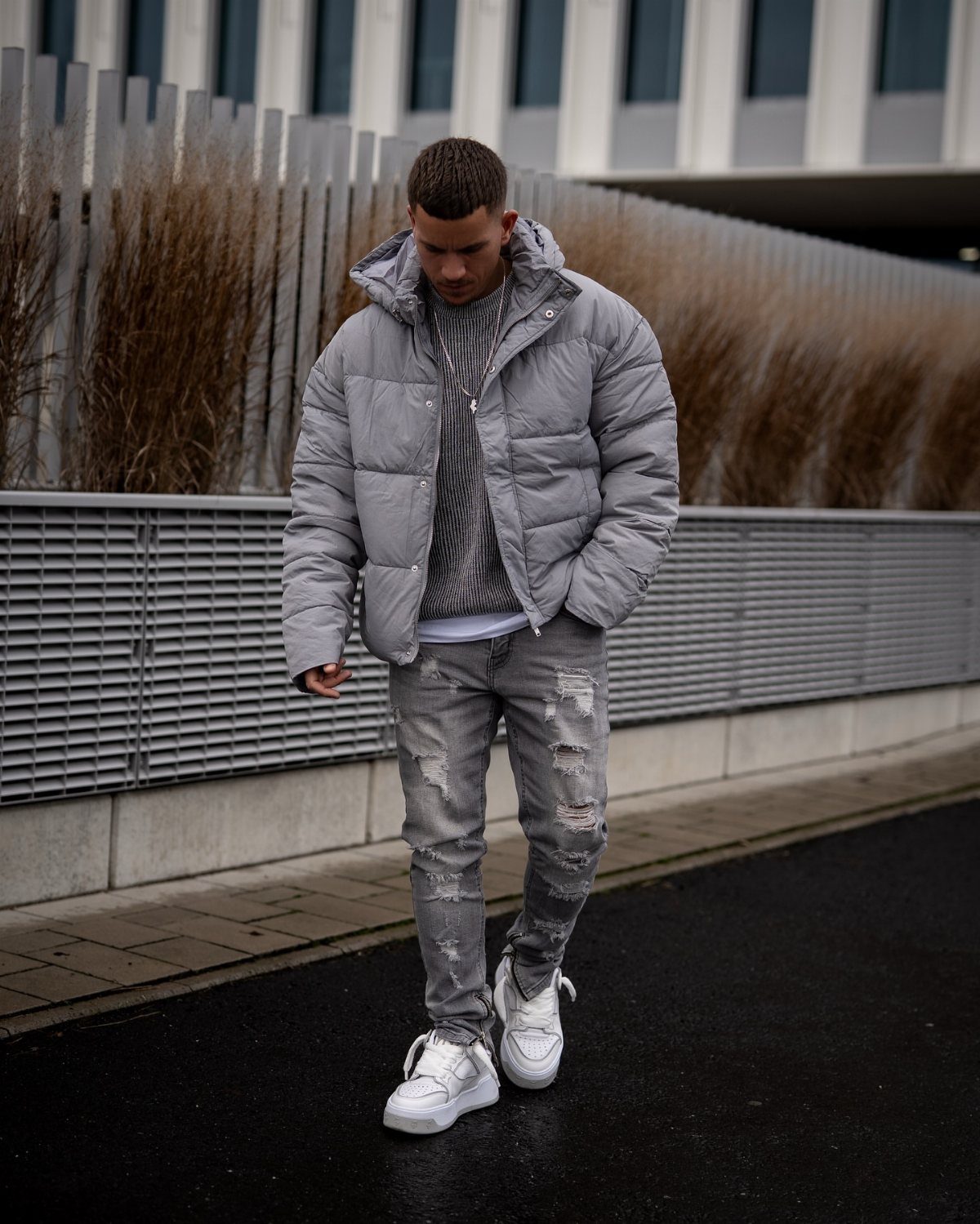 Man wearing a light grey puffer jacket with distressed grey jeans and white sneakers.