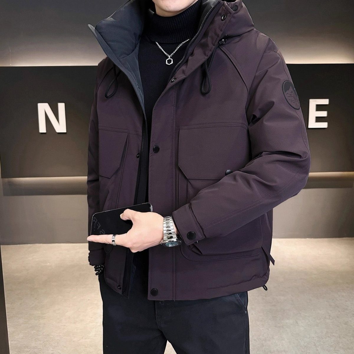 Man wearing a dark purple puffer jacket with a black turtleneck and black pants.