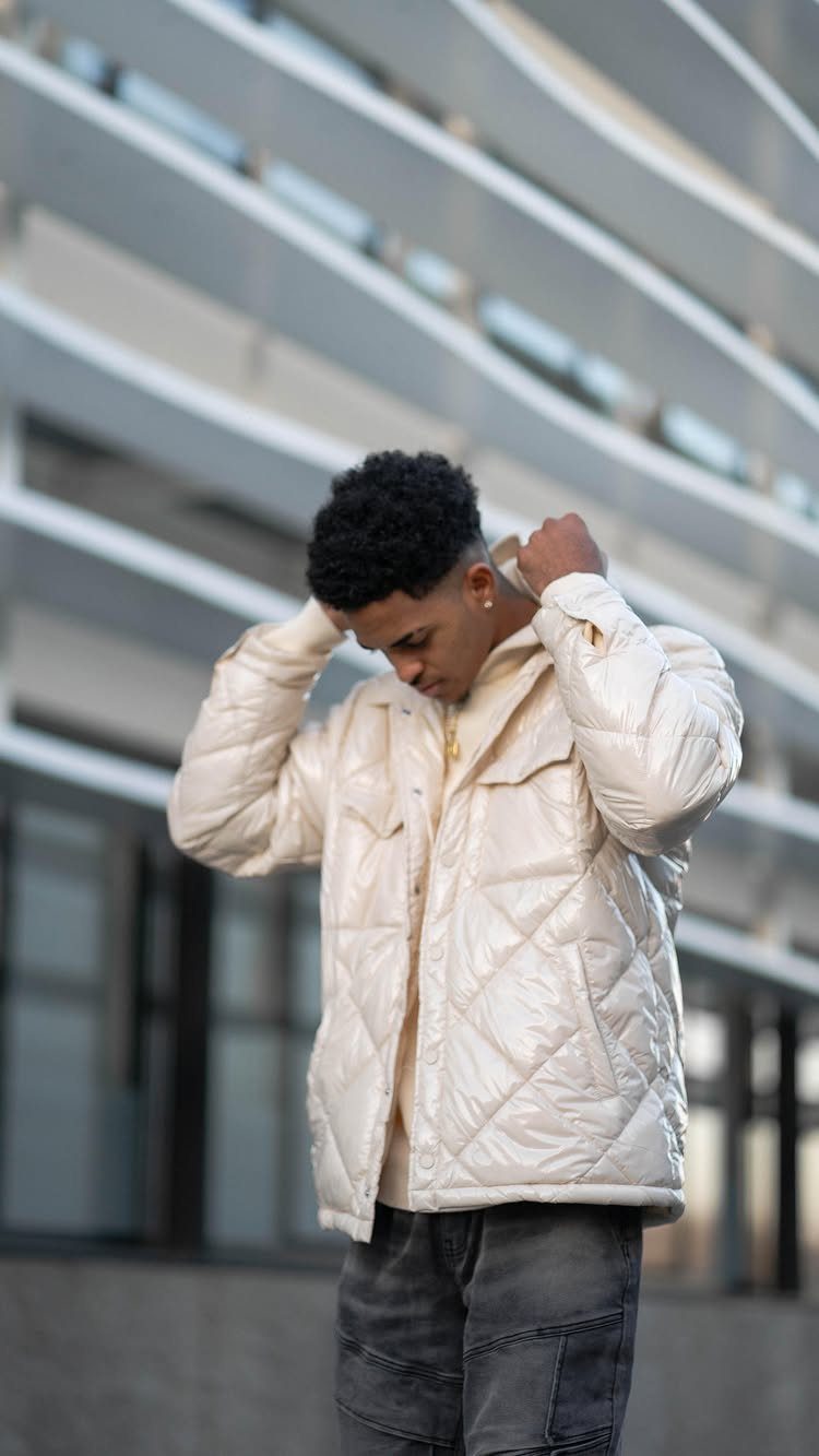 Man in white quilted puffer jacket and grey jeans posing by modern building