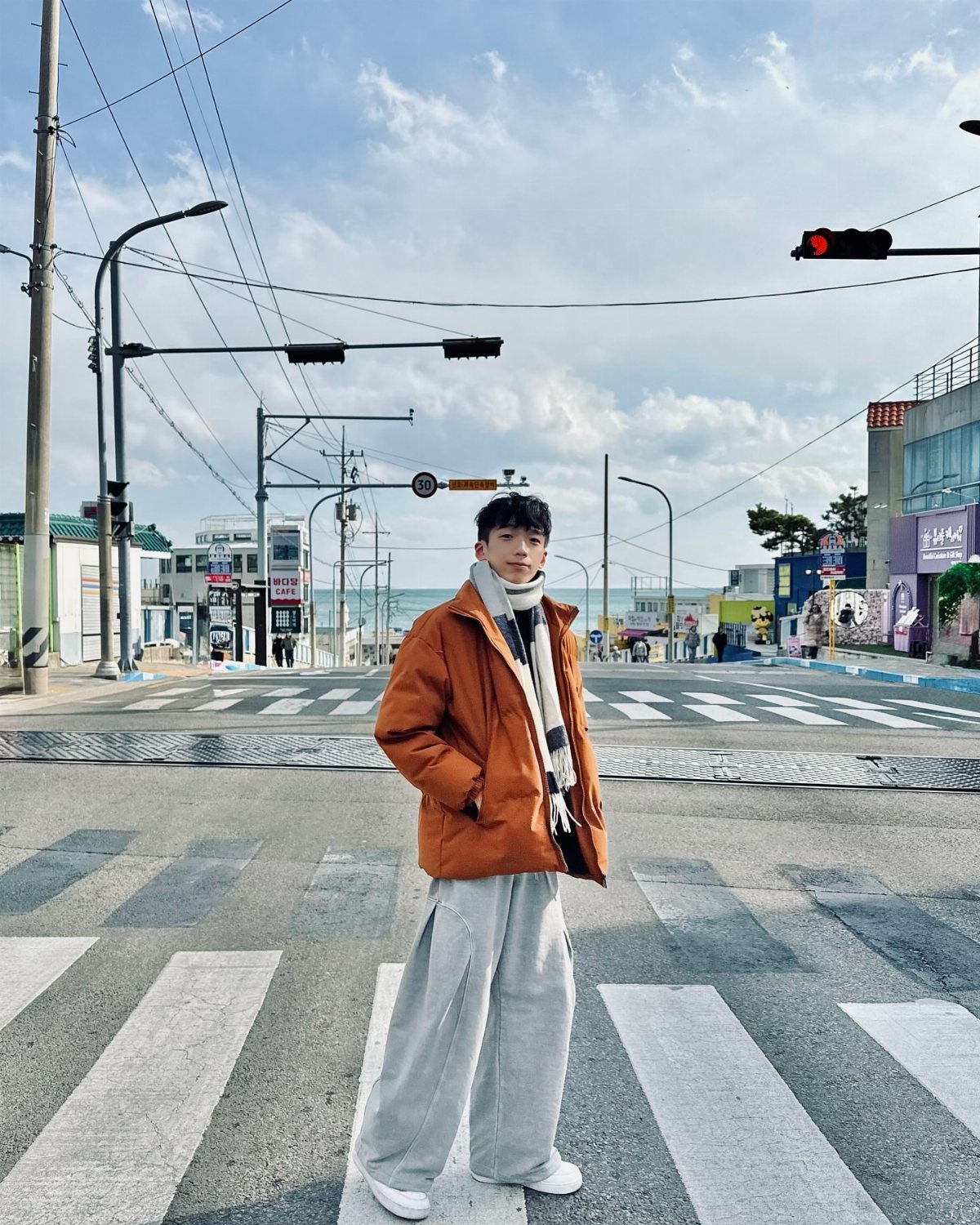 Man in orange puffer jacket and striped scarf standing on a city crosswalk