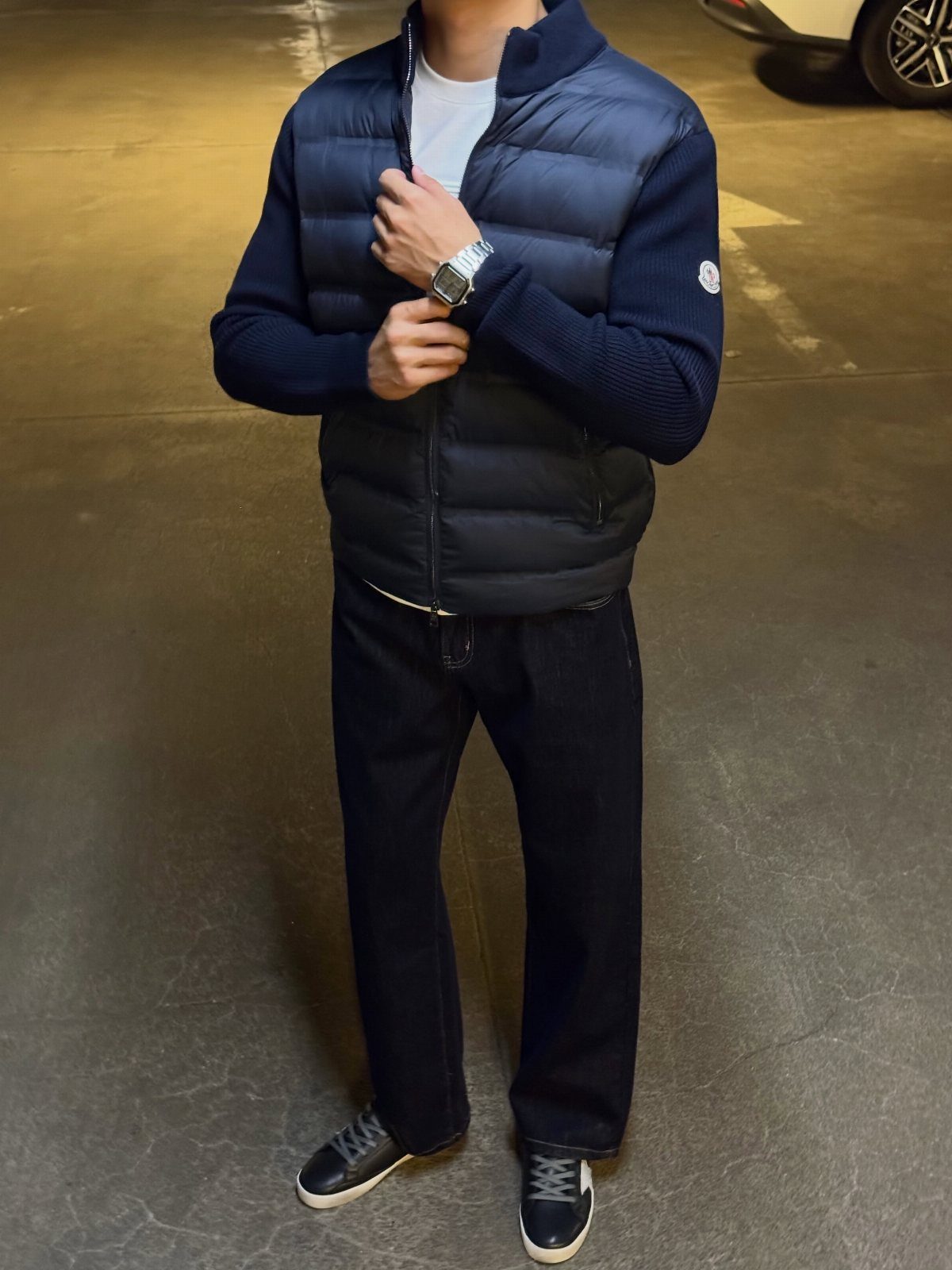 Person wearing a navy puffer vest, dark jeans, and black leather sneakers.