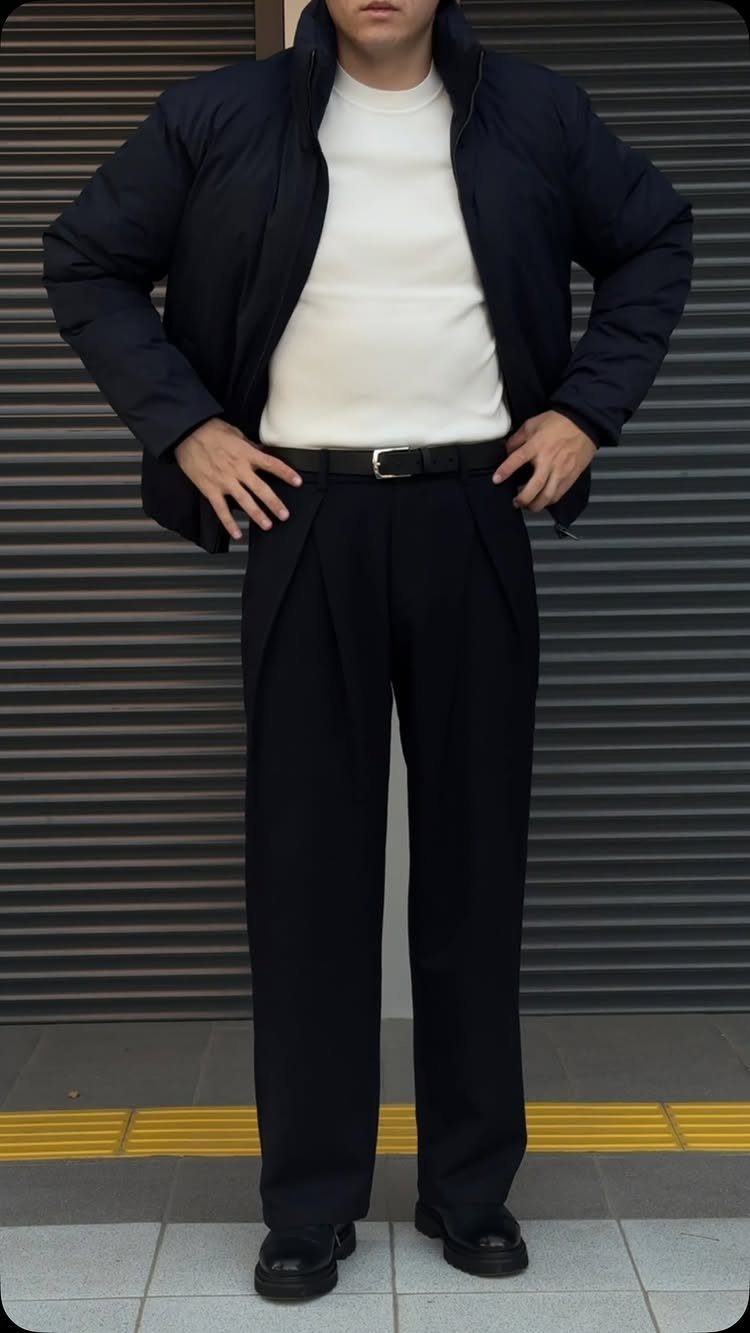Person wearing a navy puffer jacket, white sweater, and black tailored trousers.