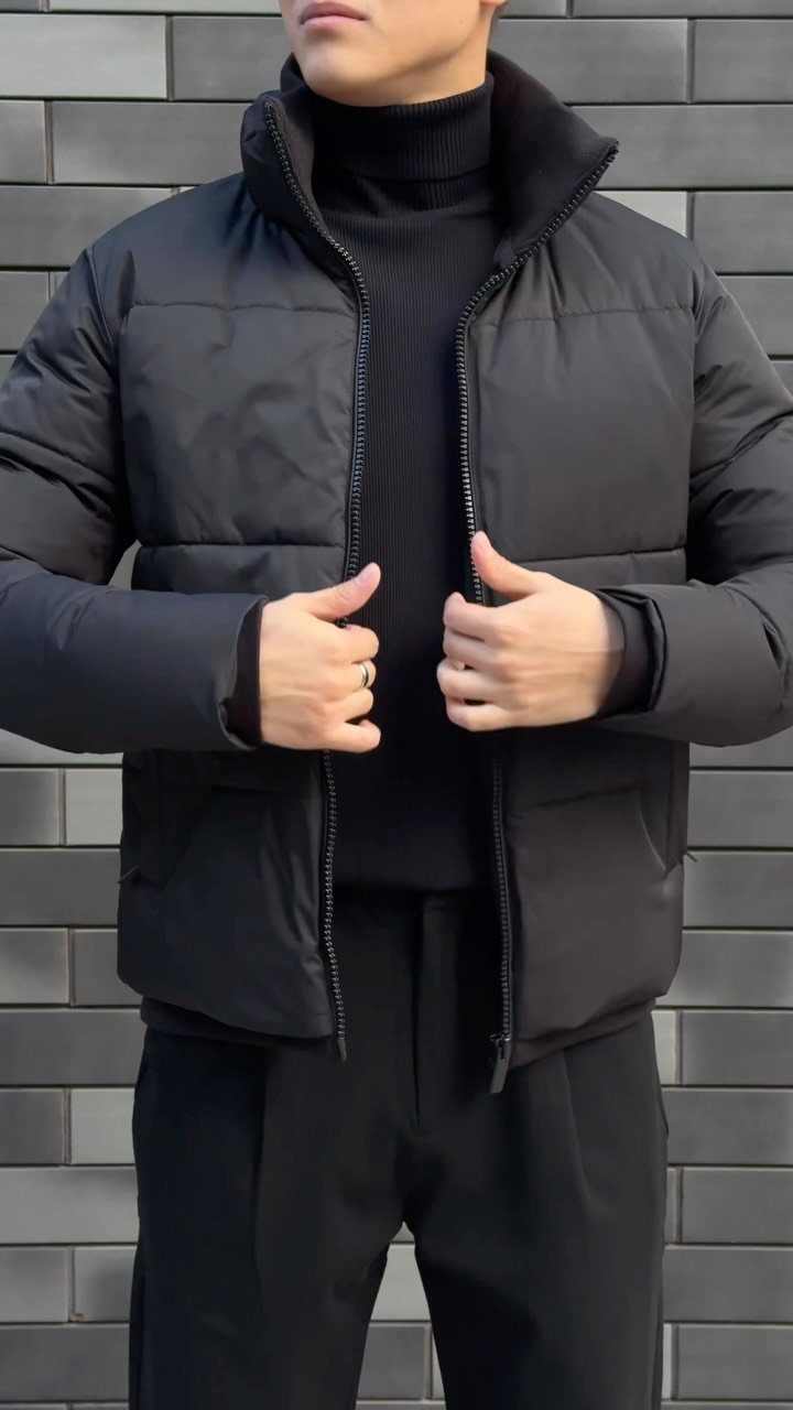 Man wearing a black puffer jacket over a black turtleneck and black trousers.
