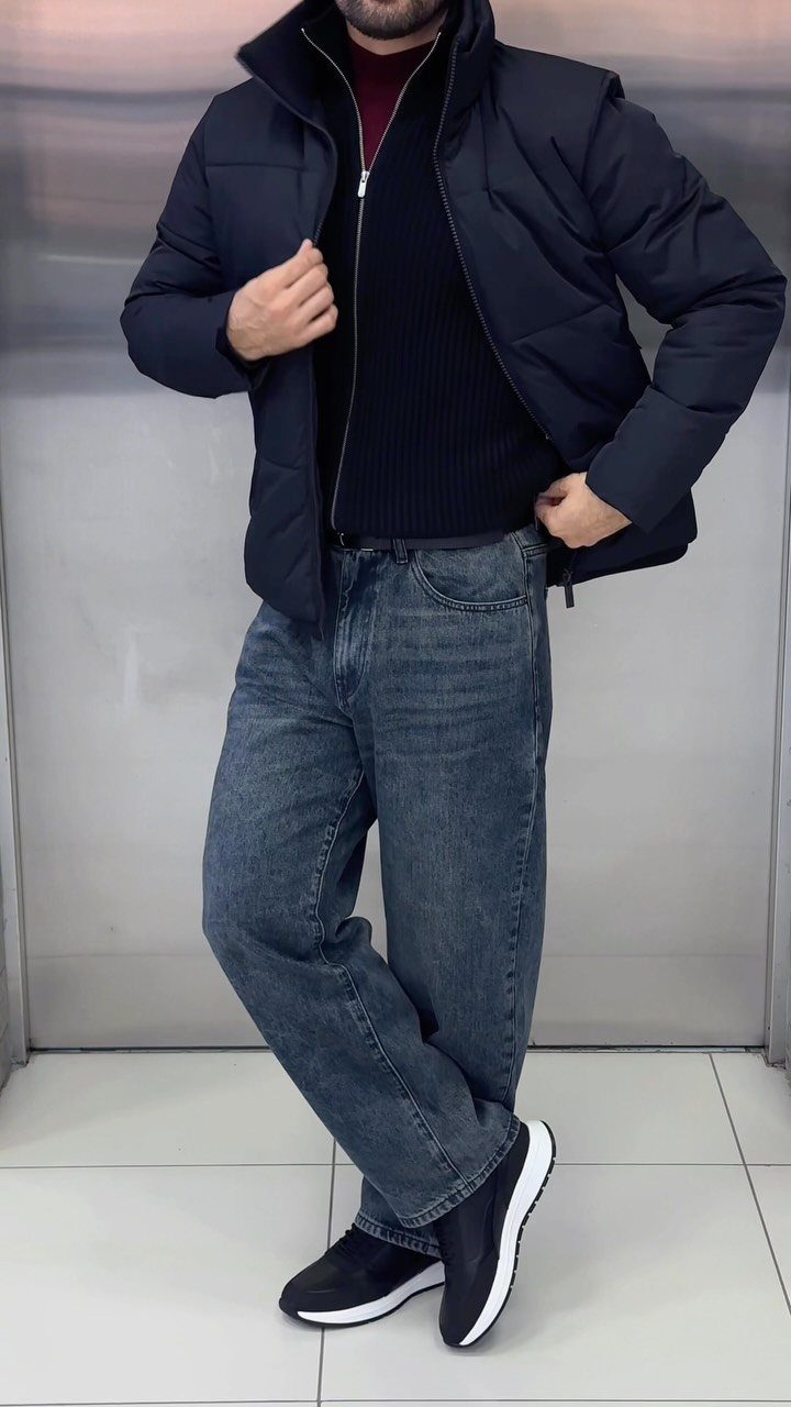 Man wearing a navy puffer jacket layered over a black sweater and jeans.