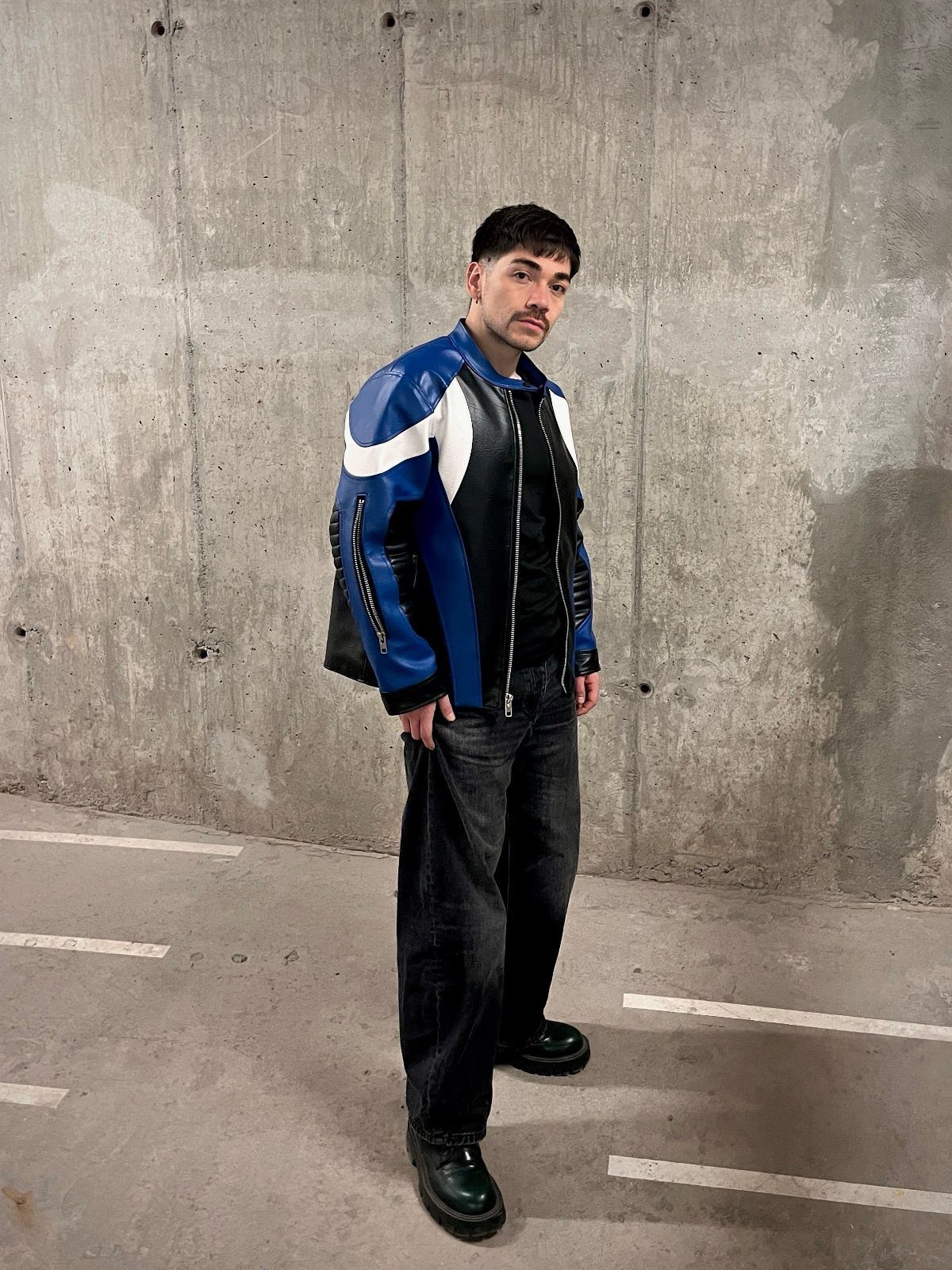 Man wearing a blue and white racer jacket with wide dark grey jeans.