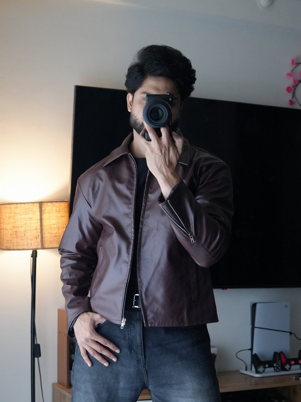 Man in brown leather racer jacket and grey jeans taking a mirror selfie