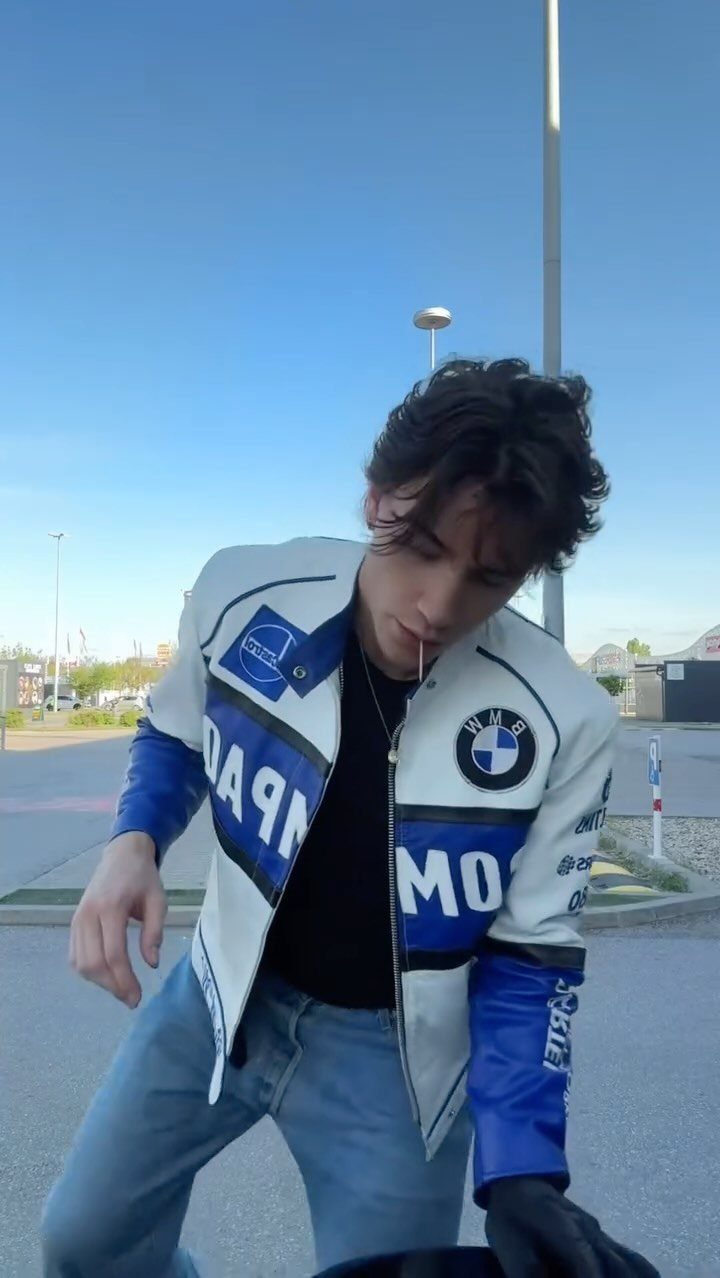Man wearing a white and blue BMW leather racer jacket and blue jeans.