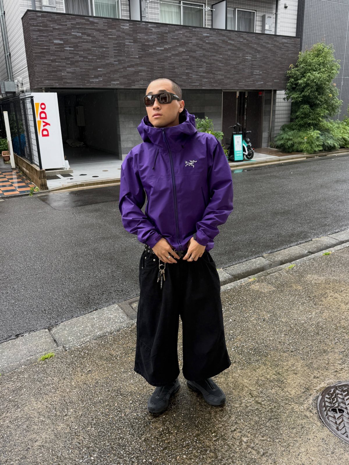Person in purple hooded jacket and wide black trousers on a wet street