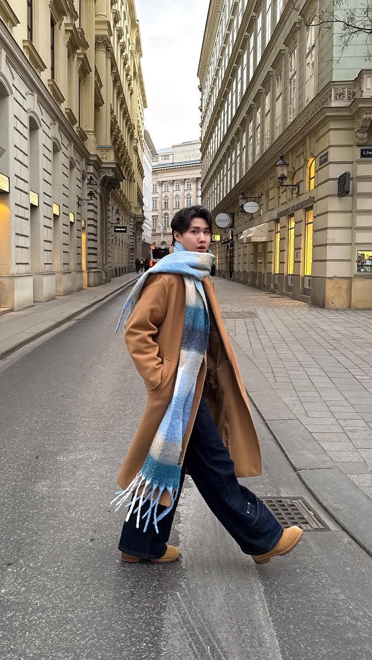 Man in a tan trench coat and blue plaid scarf walking on city street