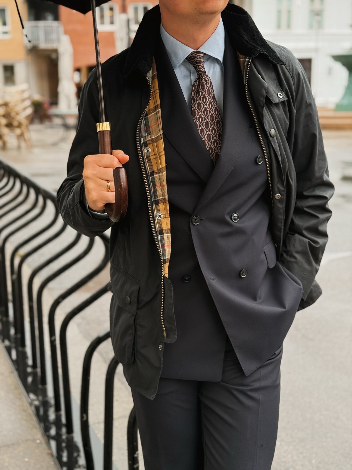 Man in a navy suit and black waterproof jacket holding a black umbrella