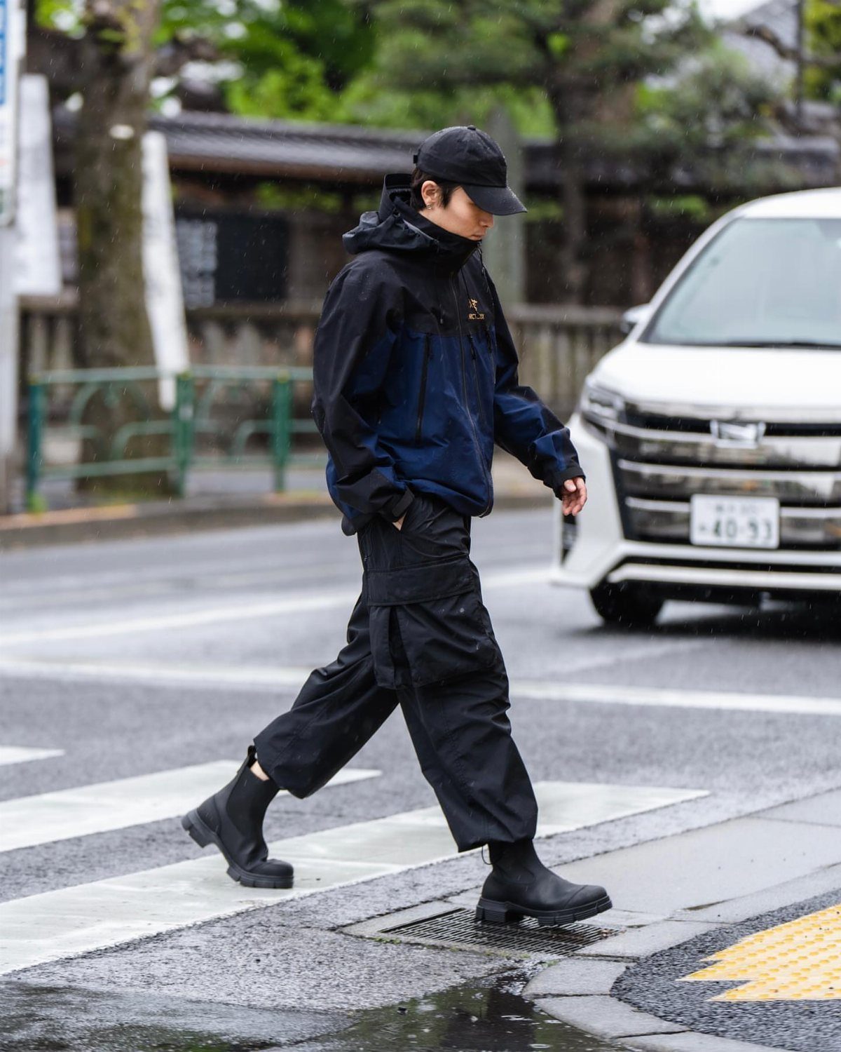 Person in waterproof jacket and black boots walking across a wet street