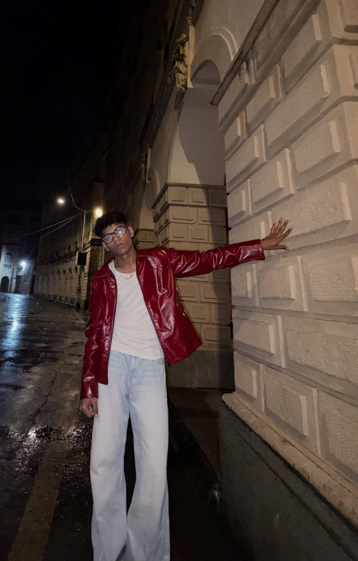 Person in red leather jacket, white t-shirt, and light blue jeans posing outdoors.