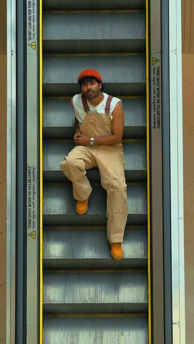 Man in tan overalls and yellow shoes sitting on a metal escalator