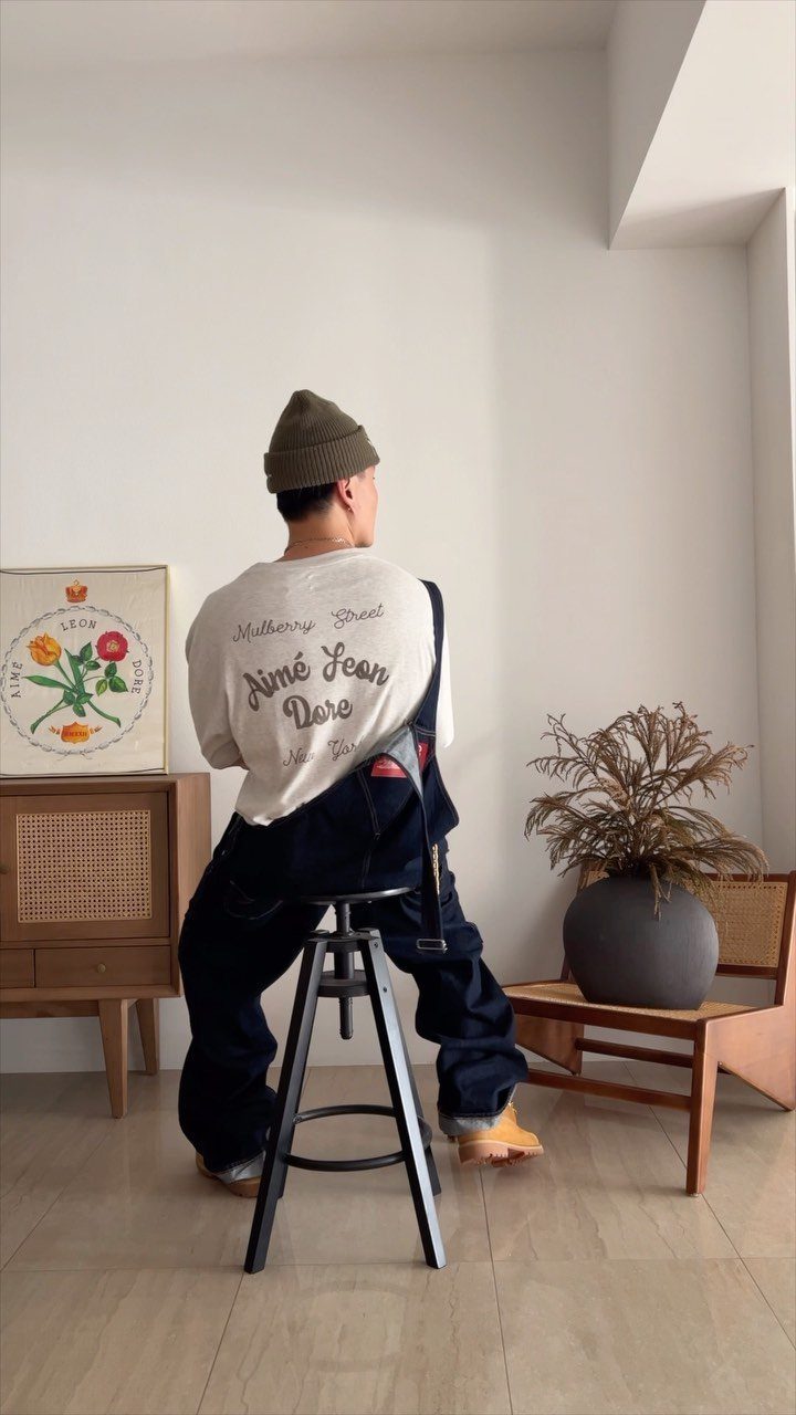 Person wearing dark blue overalls and tan shoes sitting on a black stool.