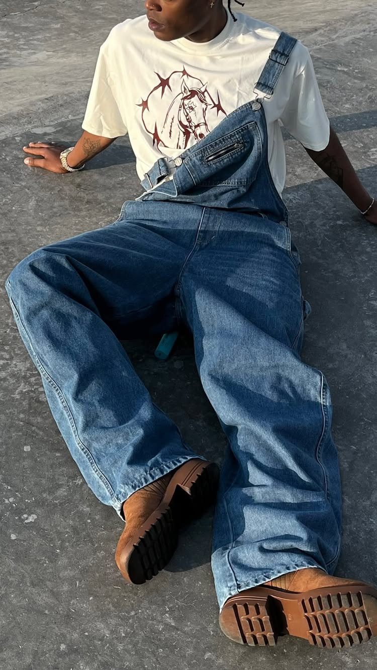 Person wearing blue denim overalls and chunky brown leather boots sitting on concrete.