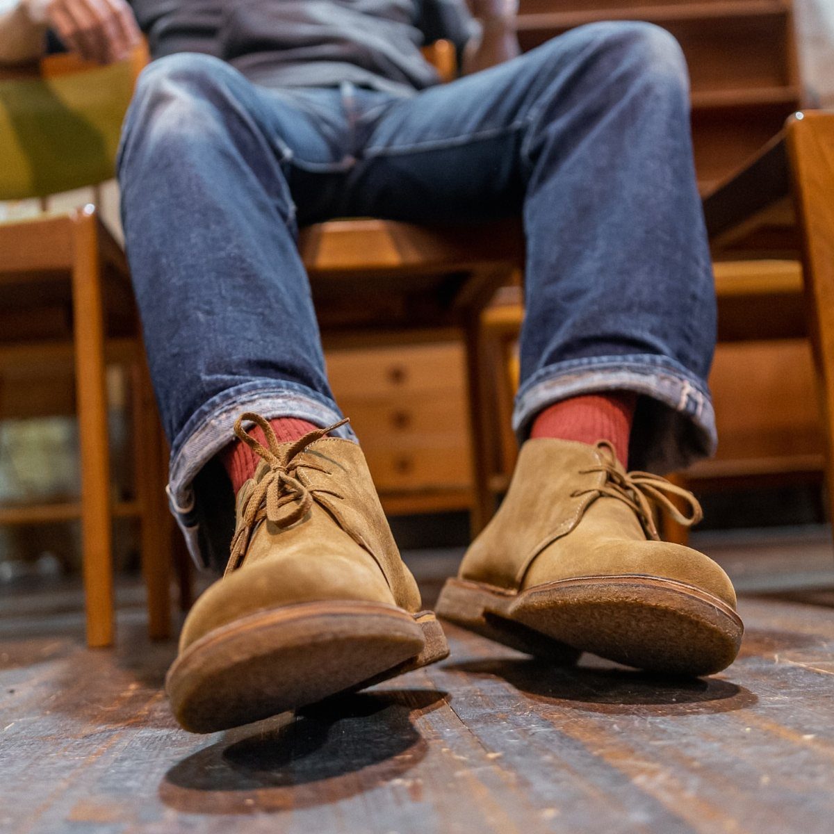 Tan suede desert boots with orange socks and cuffed blue jeans on wooden floor