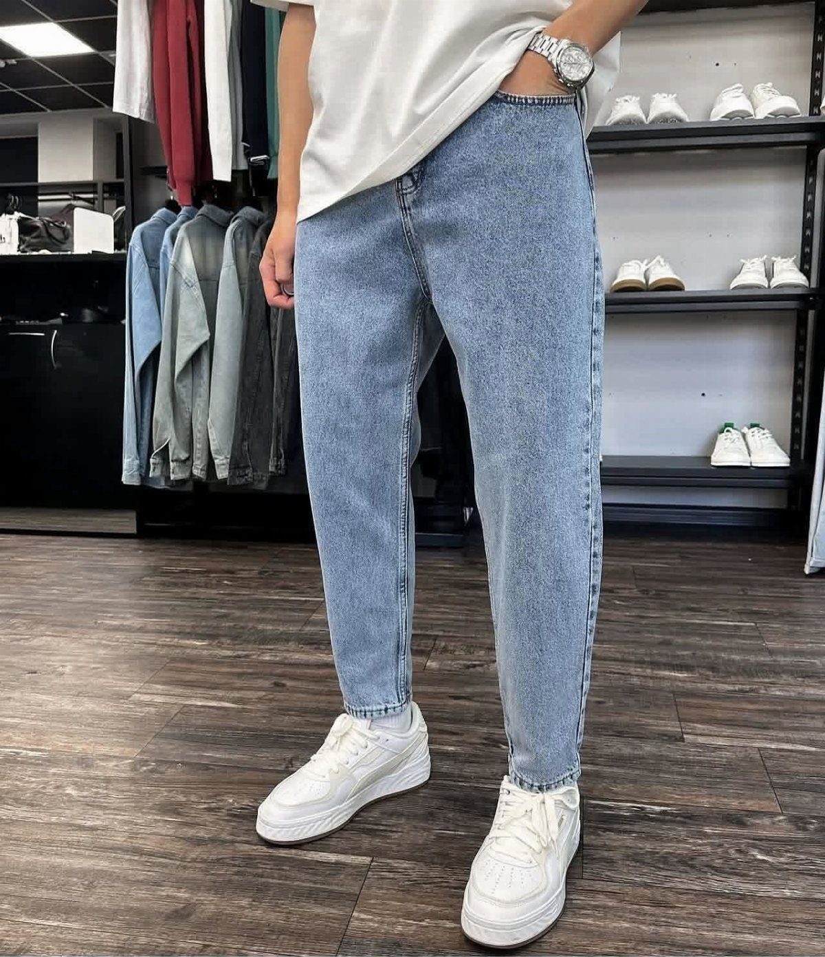 Man wearing light wash blue jeans, white t-shirt, and white sneakers in store.