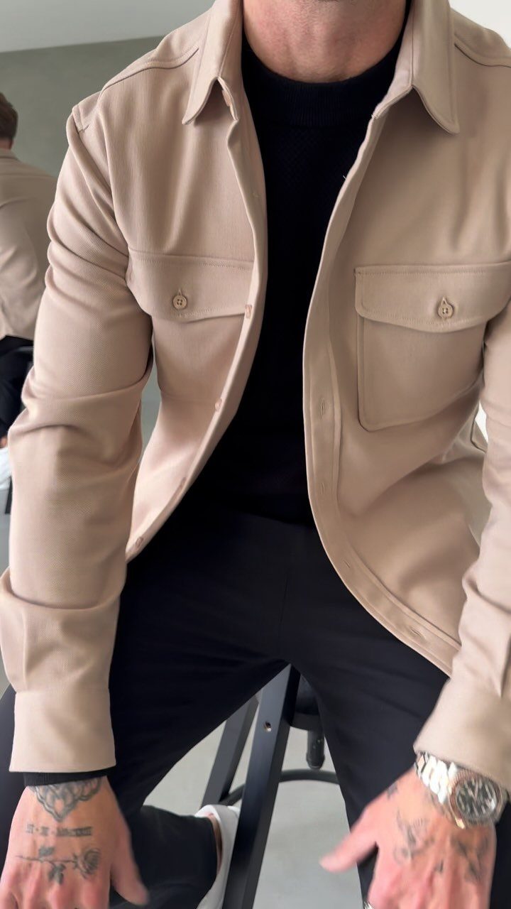 Man wearing a beige overshirt over a black t-shirt and black trousers.