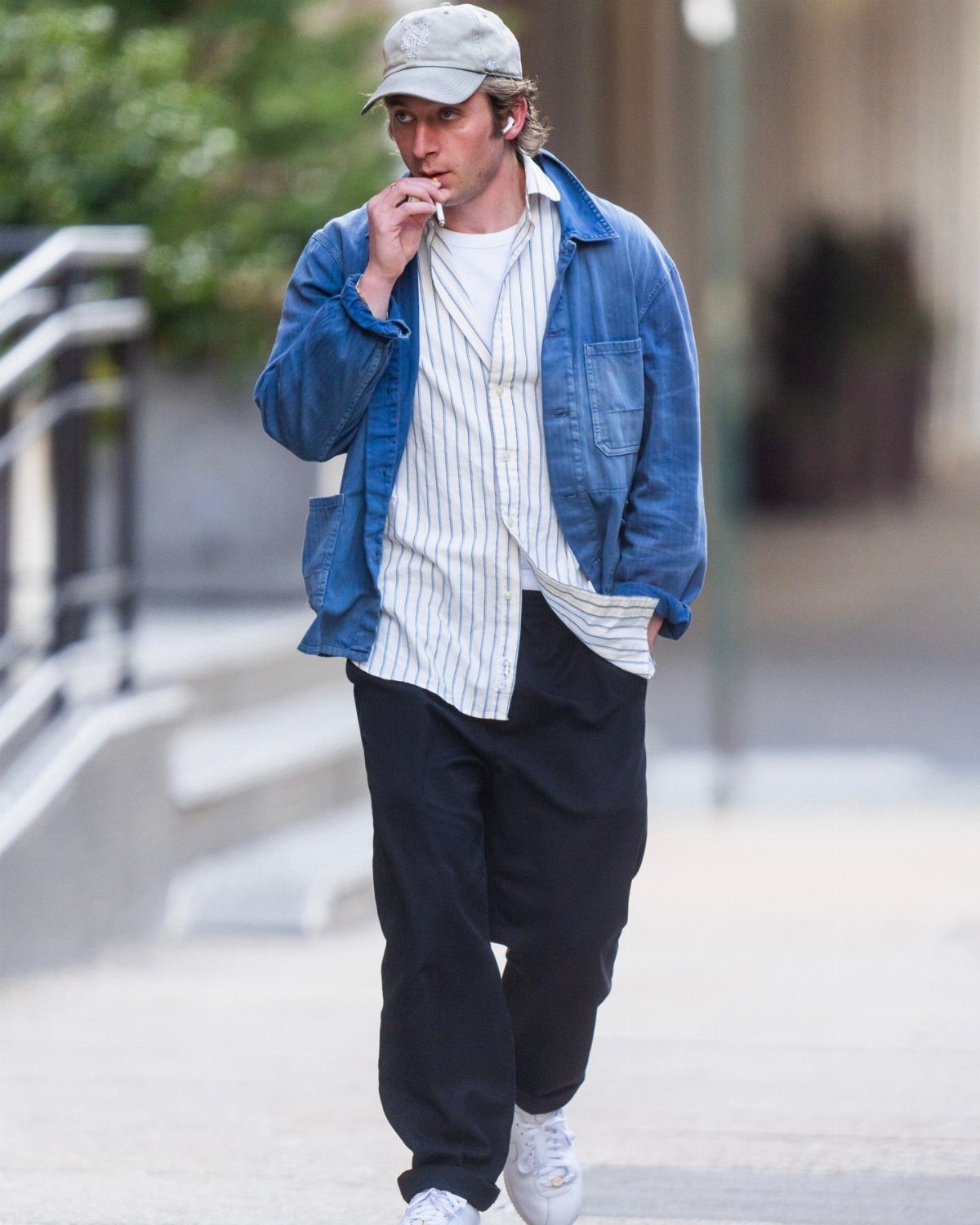 Man wearing a blue chore coat, striped shirt, and black trousers walking outdoors.