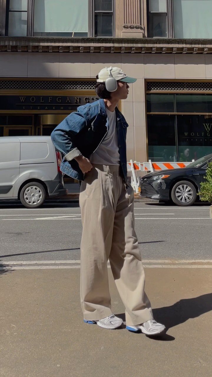 Man wearing a blue denim jacket and beige wide-leg trousers on a city street.
