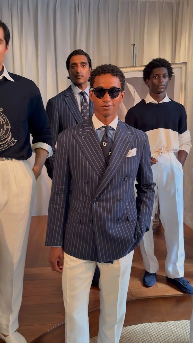 Man in navy pinstripe double-breasted blazer and white trousers posing with other men.