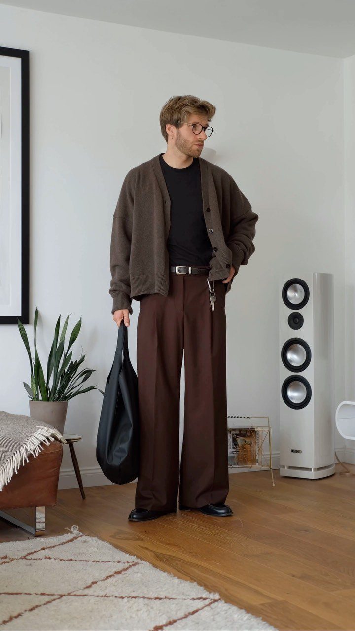 Man wearing a brown cardigan and wide-leg brown trousers in a modern room.