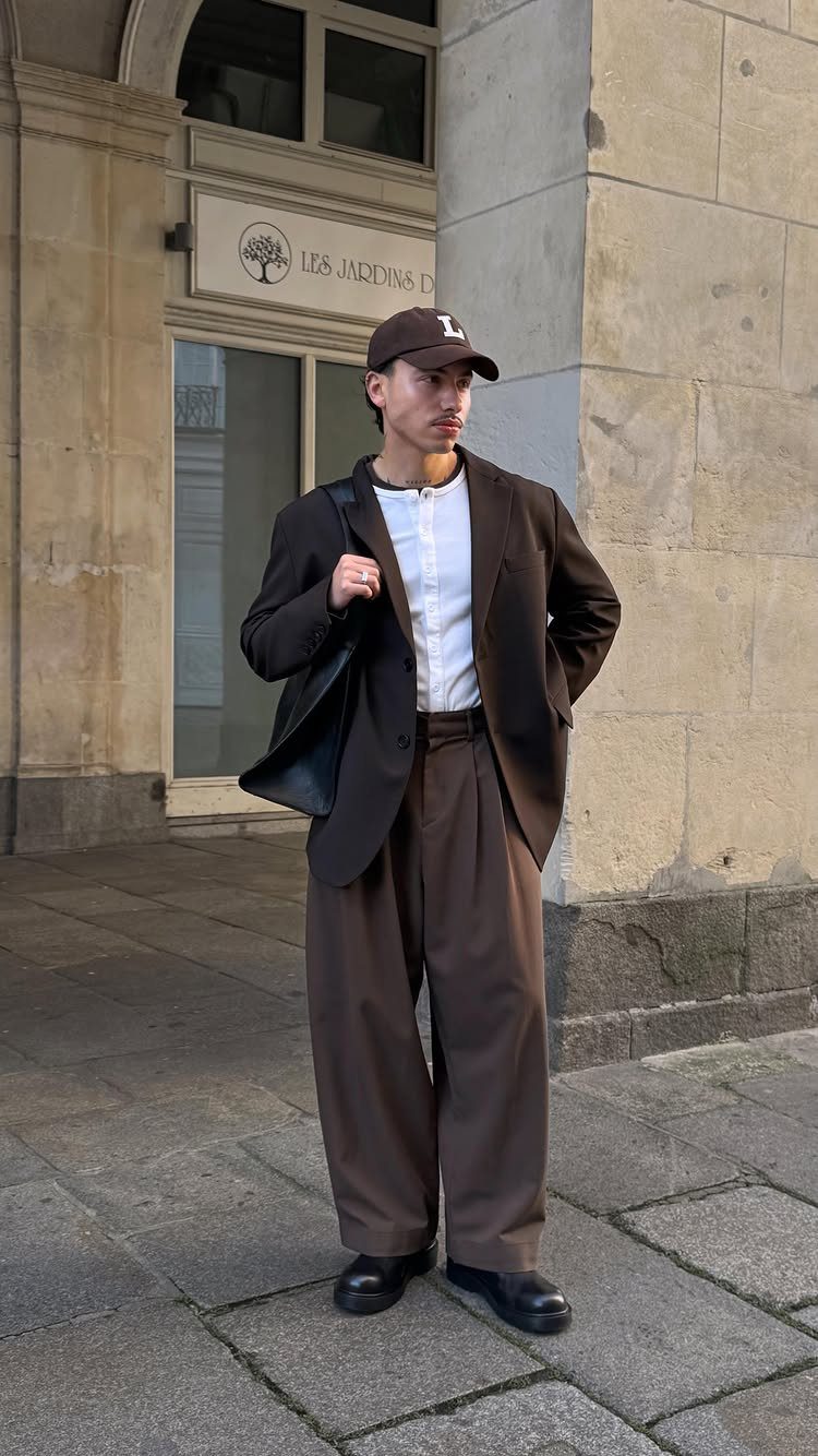 Man in brown blazer and wide-leg brown trousers standing on a city sidewalk.