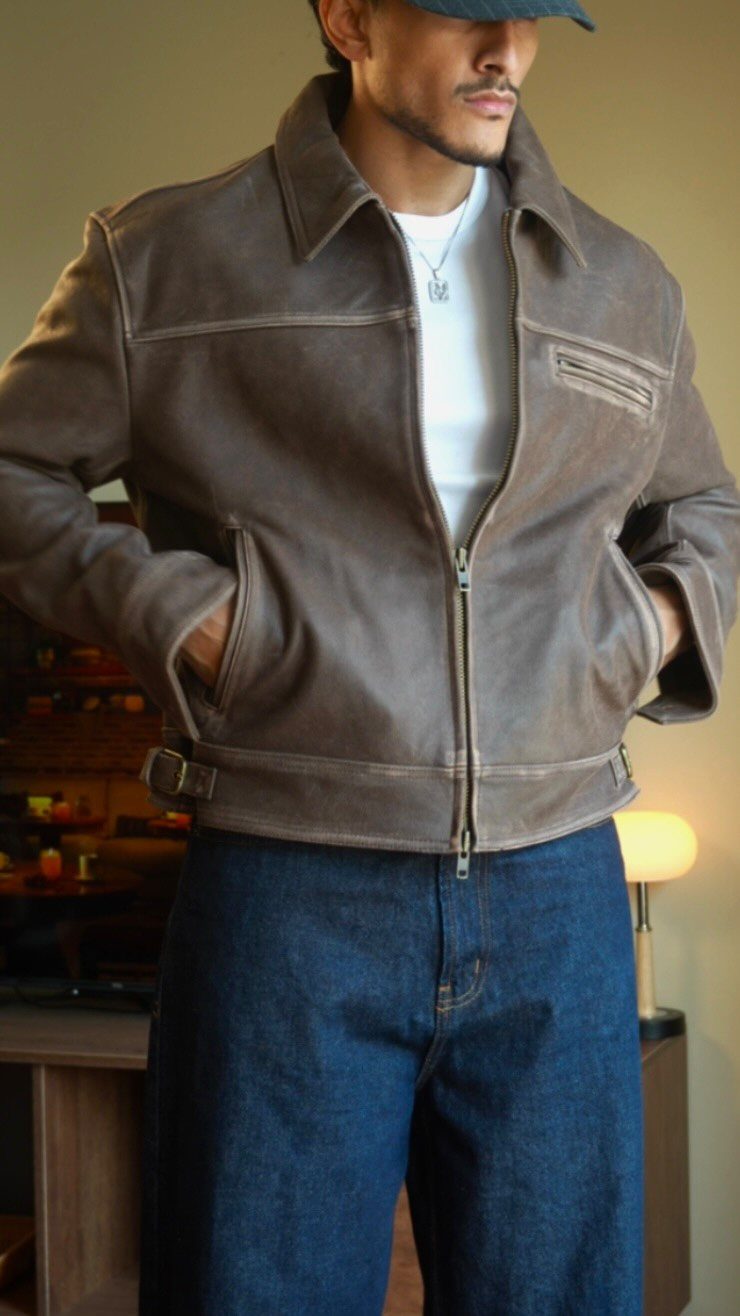 Man wearing a brown leather fall jacket, white t-shirt, and dark blue jeans.