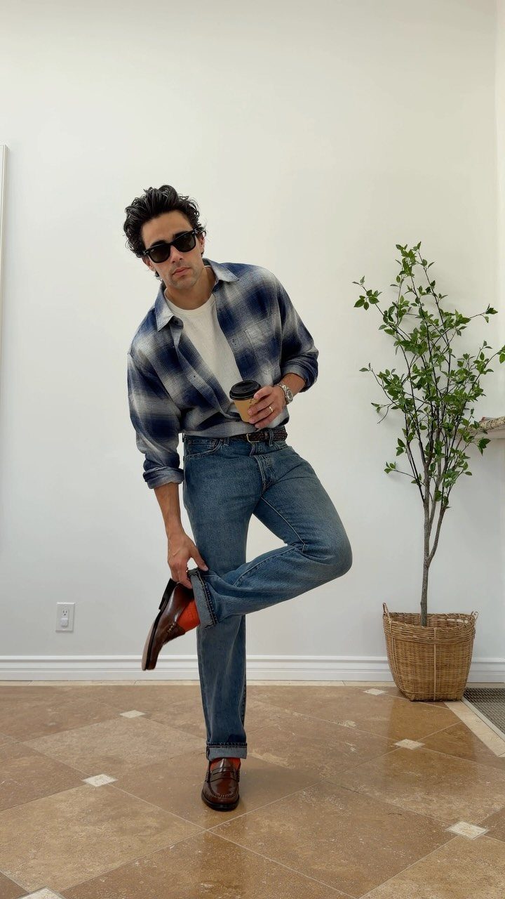 Man in blue plaid flannel shirt and jeans posing with a coffee cup.