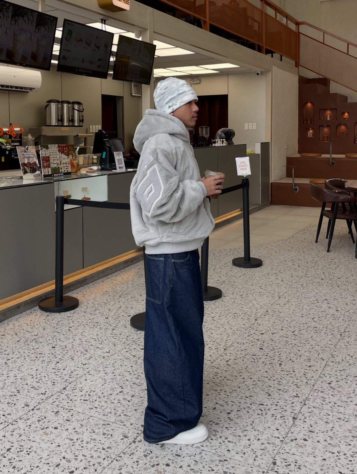 Person wearing a grey fleece hoodie, white beanie, and dark blue wide-leg jeans.