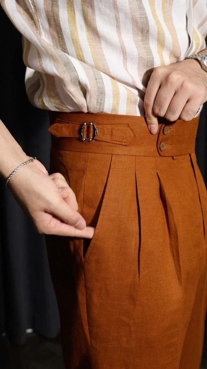 Rust-orange pleated trousers paired with a striped cream shirt in autumn style.