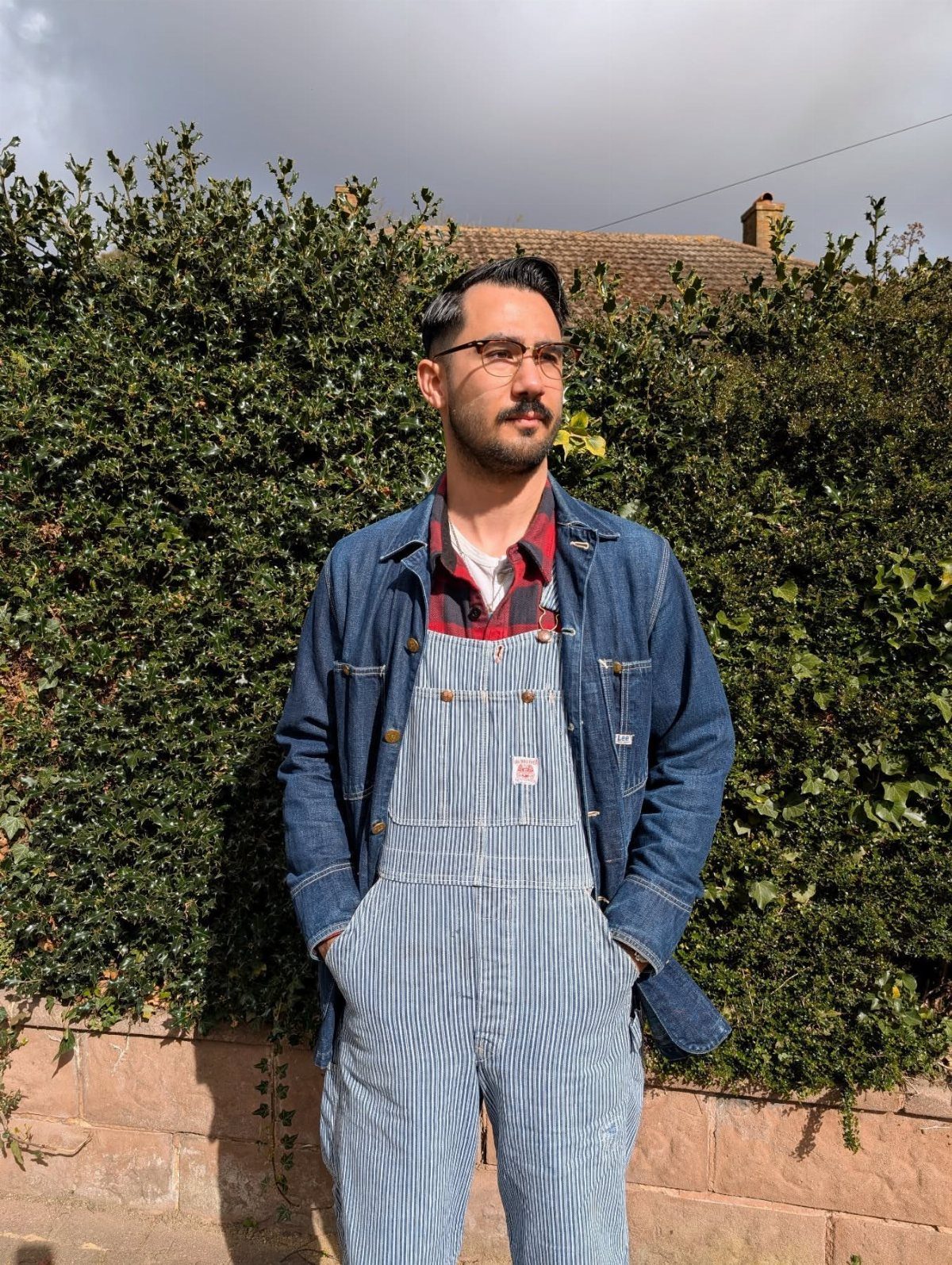 Man wearing striped overalls, a red flannel shirt, and a blue denim jacket.