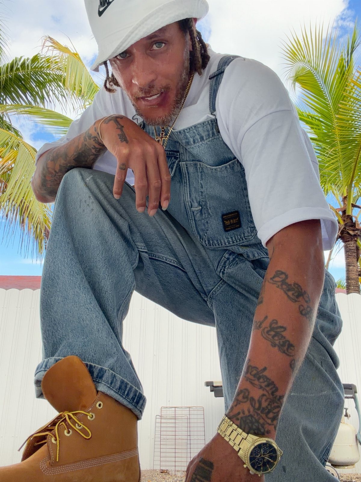 Man in blue denim overalls and tan leather work boots posing outdoors.