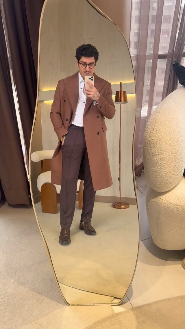 Man wearing a brown double-breasted suede trench coat and brown trousers in a mirror.