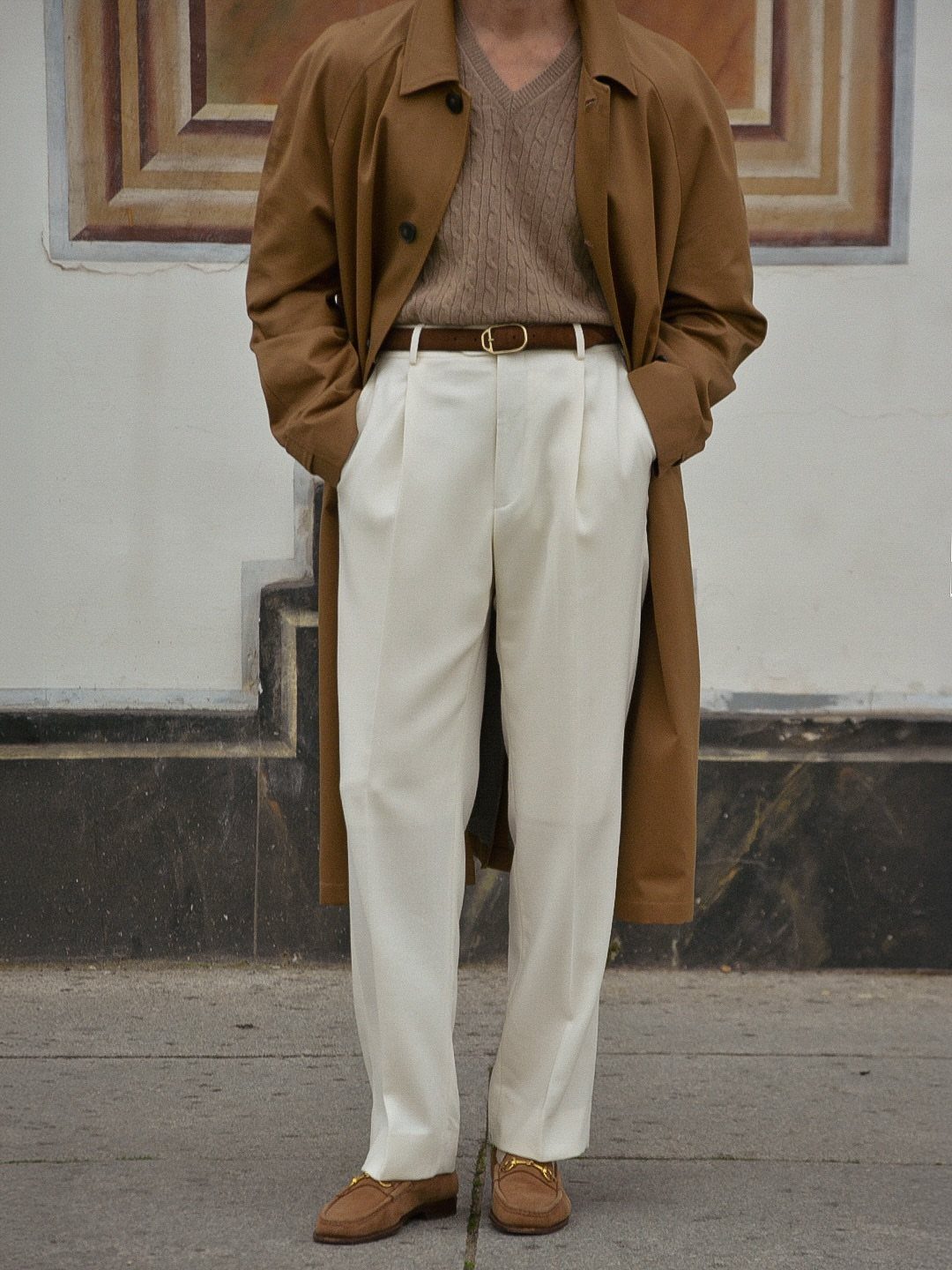 Person wearing a brown suede trench coat with white trousers and brown loafers.